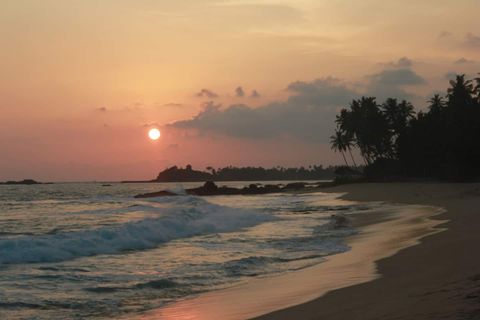 The sun setting over the sea and harbour beyond the beach at EKA Beach, Talpe