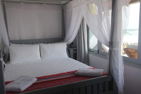 Queen bed beside a window looking straight out to the beach in Room One at EKA Beach